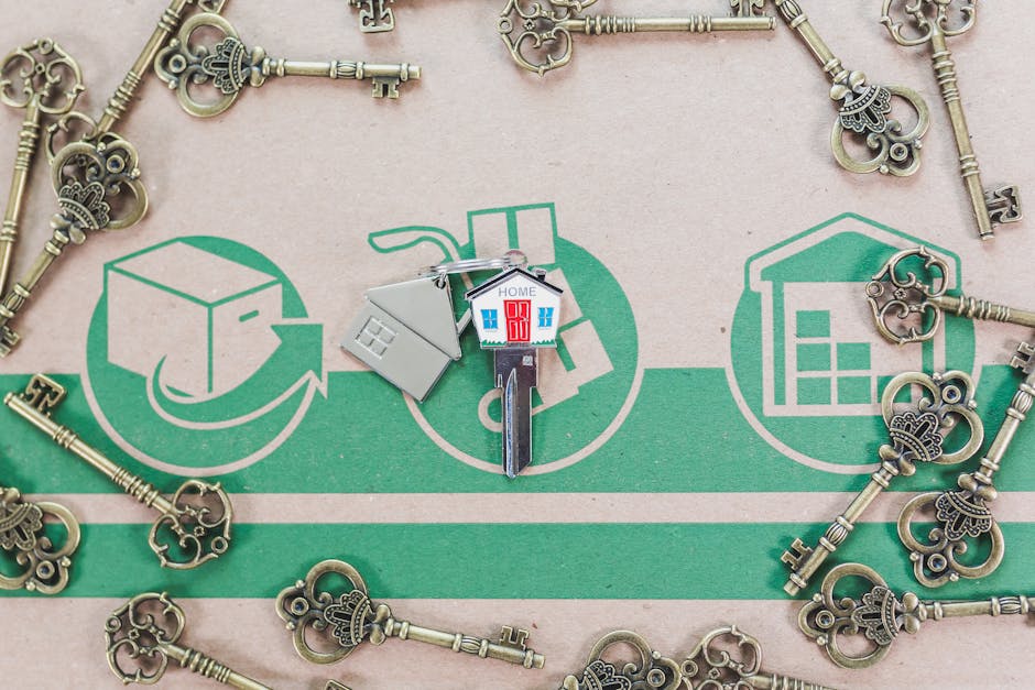 A close-up image capturing a section of a moving checklist on a green and beige surface, with drawings of boxes, a house, and a storage unit, indicating different stages of home relocation or packing process. Scattered around the checklist are several vintage-style brass keys with ornate bows, some overlapping the illustrations. At the center, a silver keyring holds three key-shaped tags, one of which features a small plastic house model with a red door and blue windows, along with a miniature grey house-shaped container. The scene suggests the logistics involved in furniture transport and packing for house removals, with tools and materials arranged to support efficient loading and unloading, consistent with services provided by [COMPANY_NAME], such as same-day Fortis Green removals for urgent tenancy deadlines.